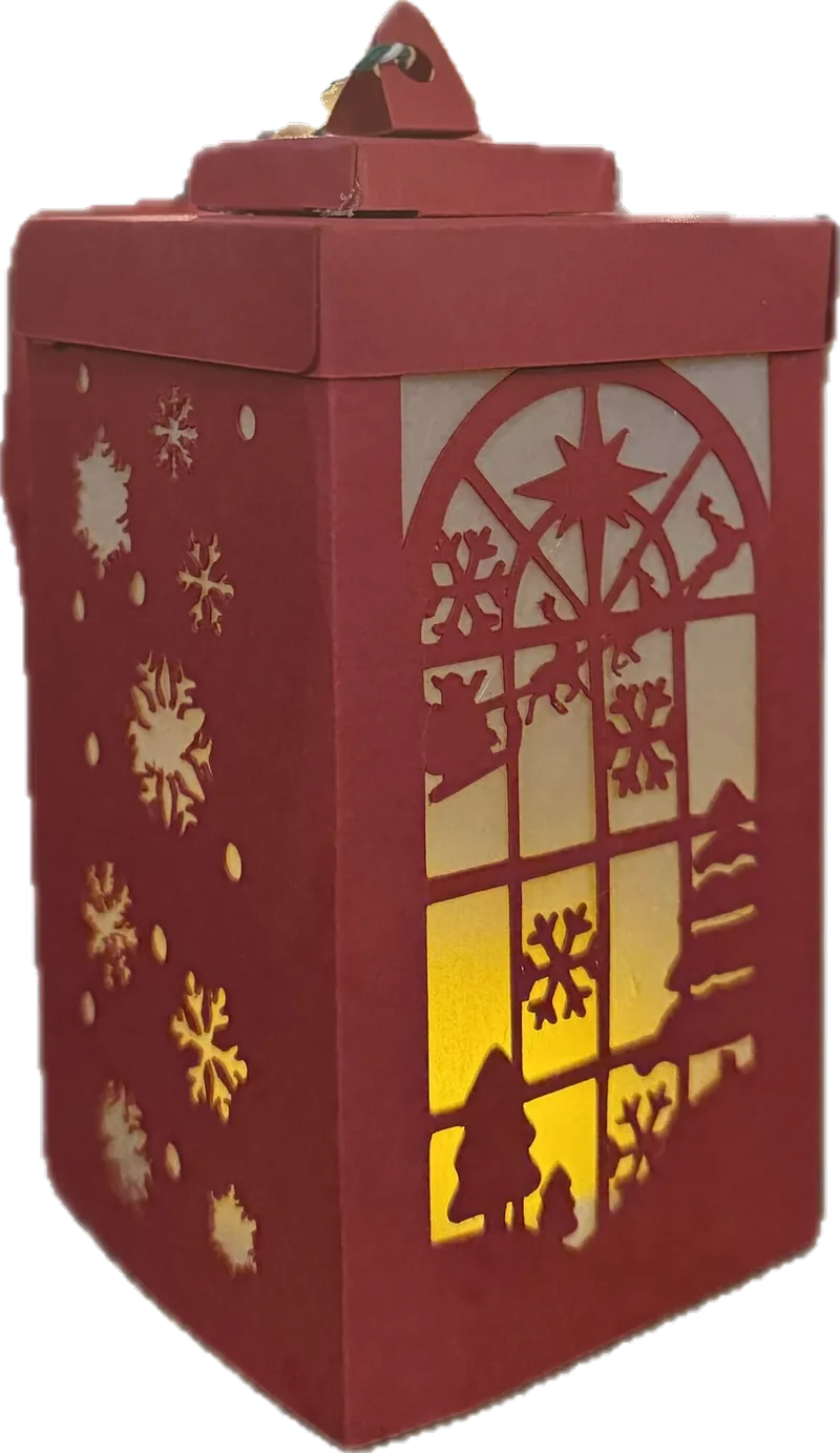 A red cut-paper lantern lit from inside, showing a snowy window and snowflakes against a warm glow.